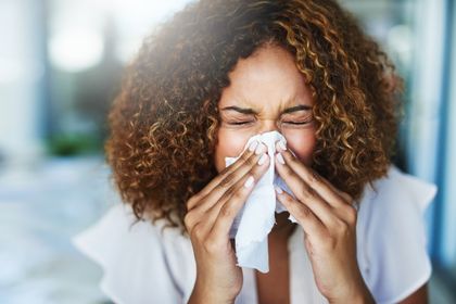 Young woman sneezes into tissue with her eyes closed
