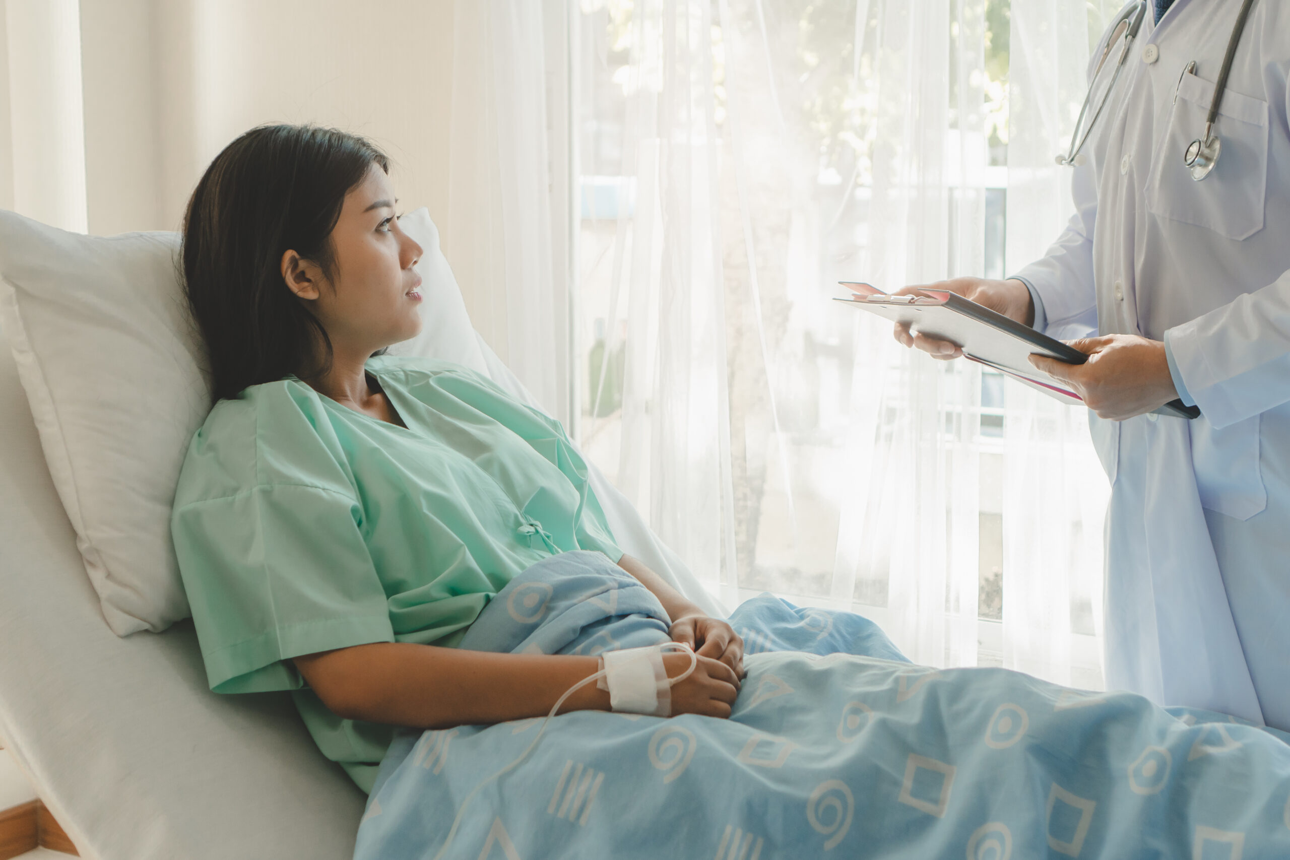 young woman sitting on the bed and looking outside window in hospital worry about her hysterectomy procedure